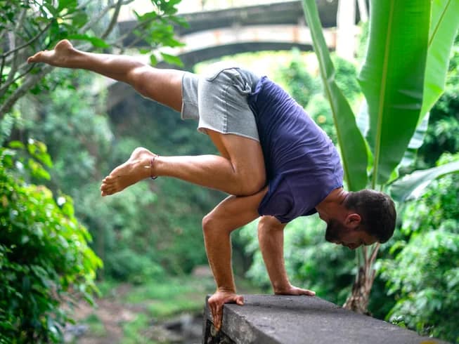 A yoga practitioner balancing on his hands amid lush tropical greenery